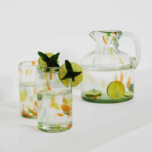 two hand blown glasses and matching pitcher with orange and yellow confetti design on white counter