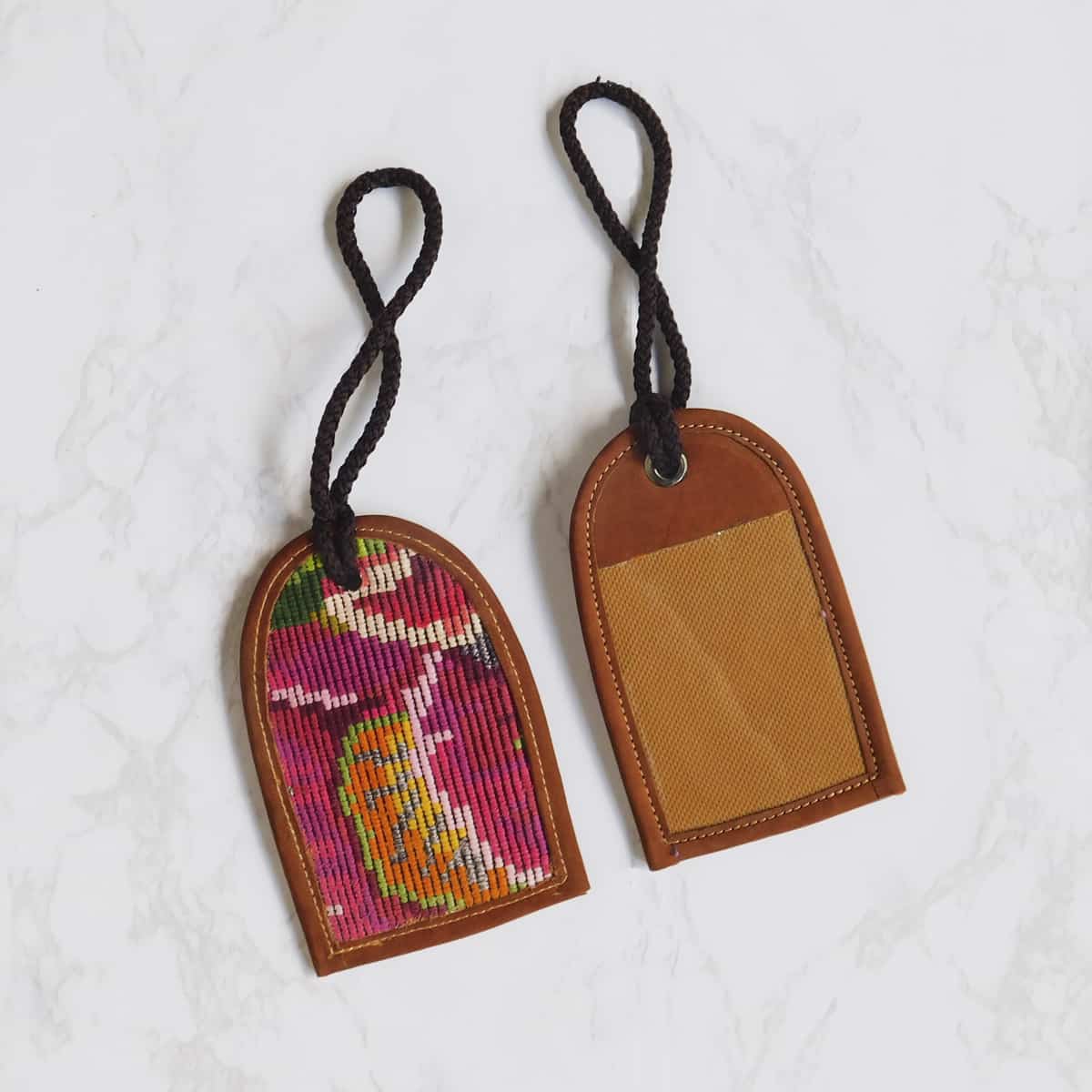handmade leather luggage tag seen from the front and the back with brocaded flowers on one side on white marble