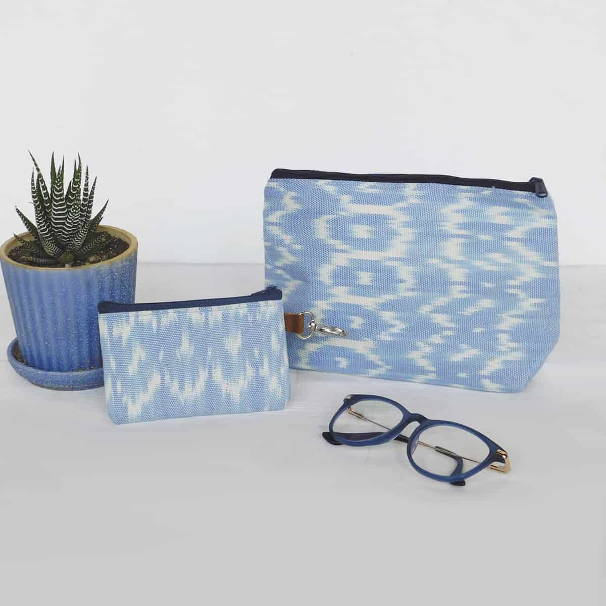 light blue makeup bag and card holder wallet with zippers on a white background with blue glasses and a succulent plant