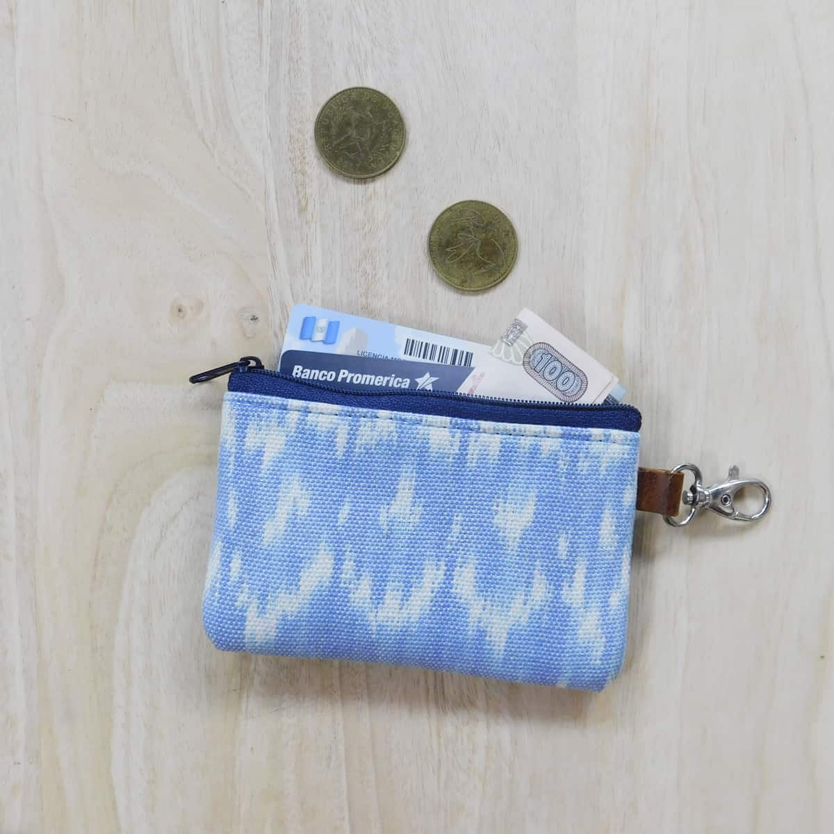 coin purse with zipper and lobster clasp for keys in light blue ikat. coins, cash and cards are partially inside.