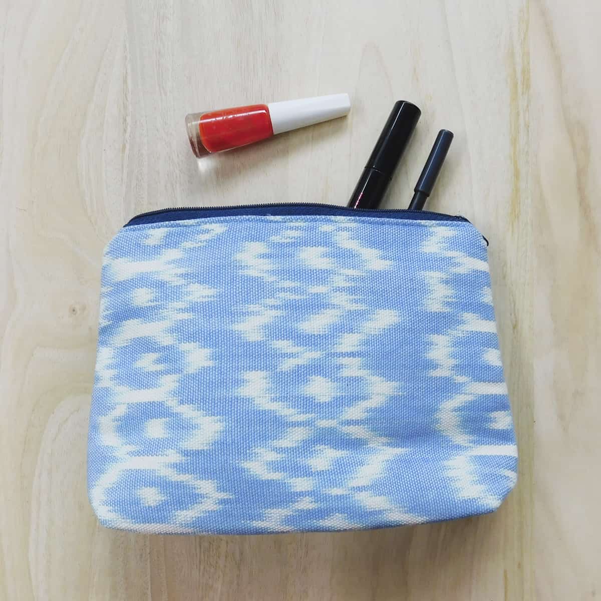 handmade makeup bag in light blue ikat fabric with nail polish, pen and eyeliner partially placed inside