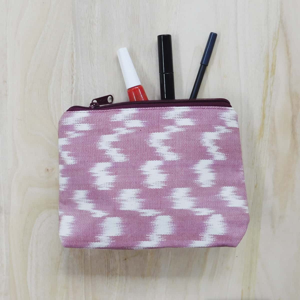 luxury cosmetic bag with pen, lip liner and nail polish partially placed inside on a light wood background