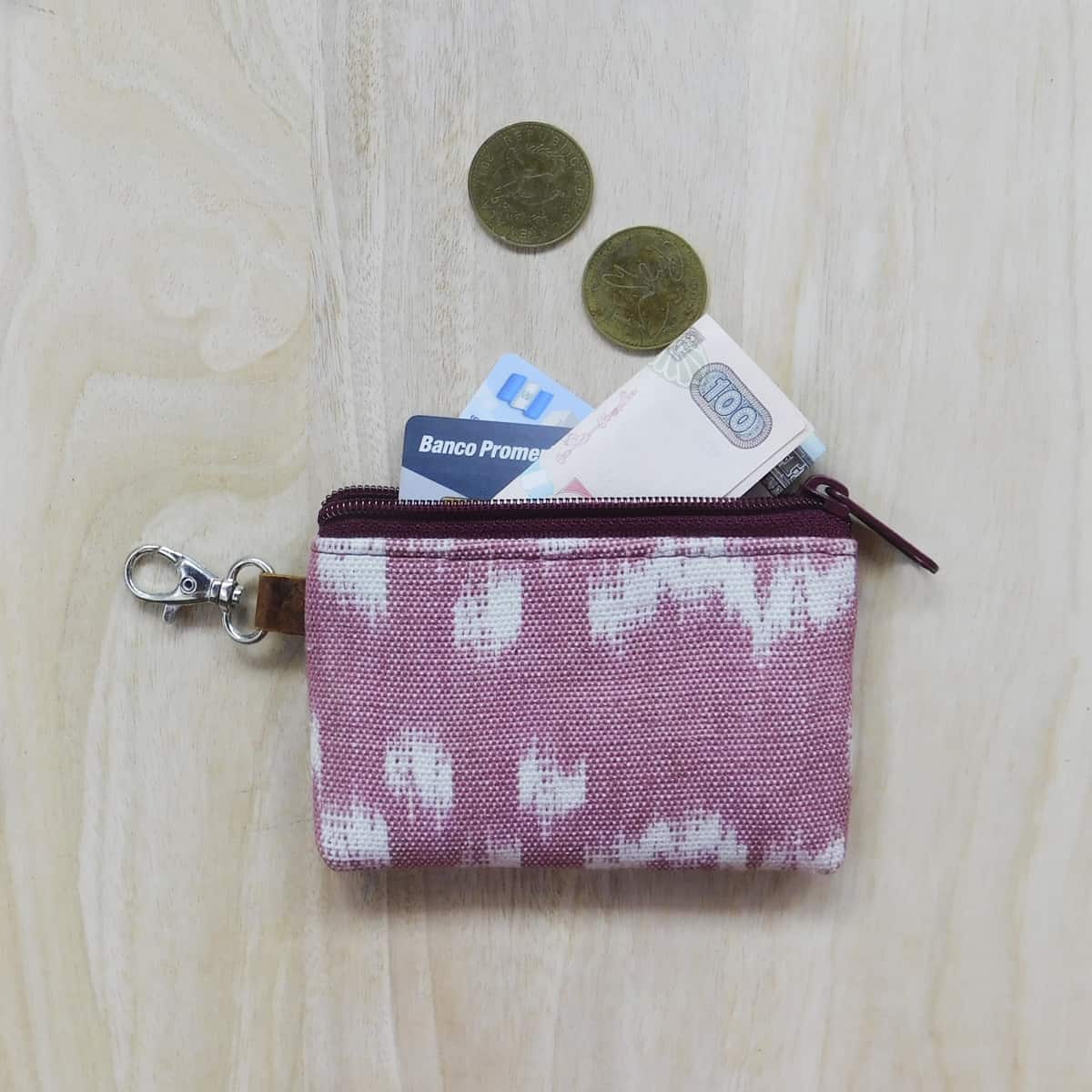 pink card holder wallet with lobster clasp for keys and zipper enclosure with cash and credit cards and coins placed partially inside