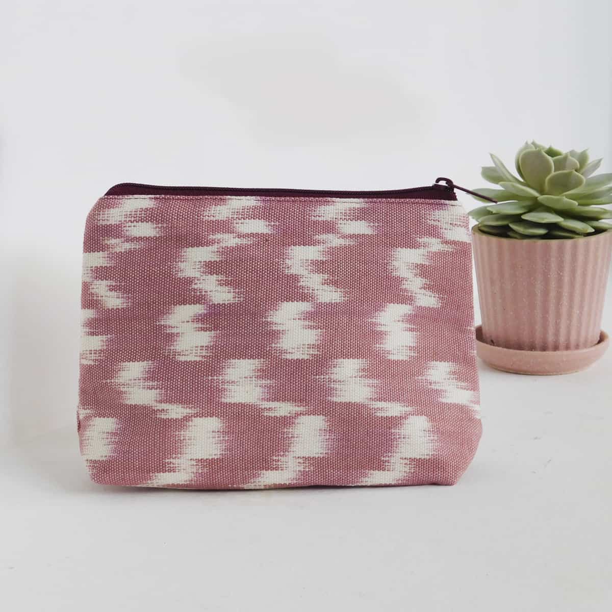 unique makeup bag with a pink ikat design with a zipper on a white background with a succulent plant next to it