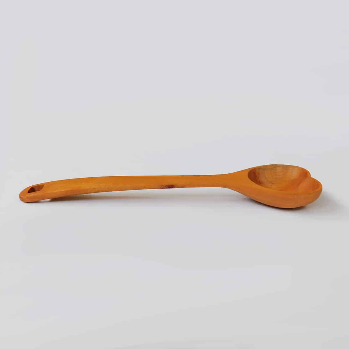 a handcarved wooden spoon seen from the side on a white surface