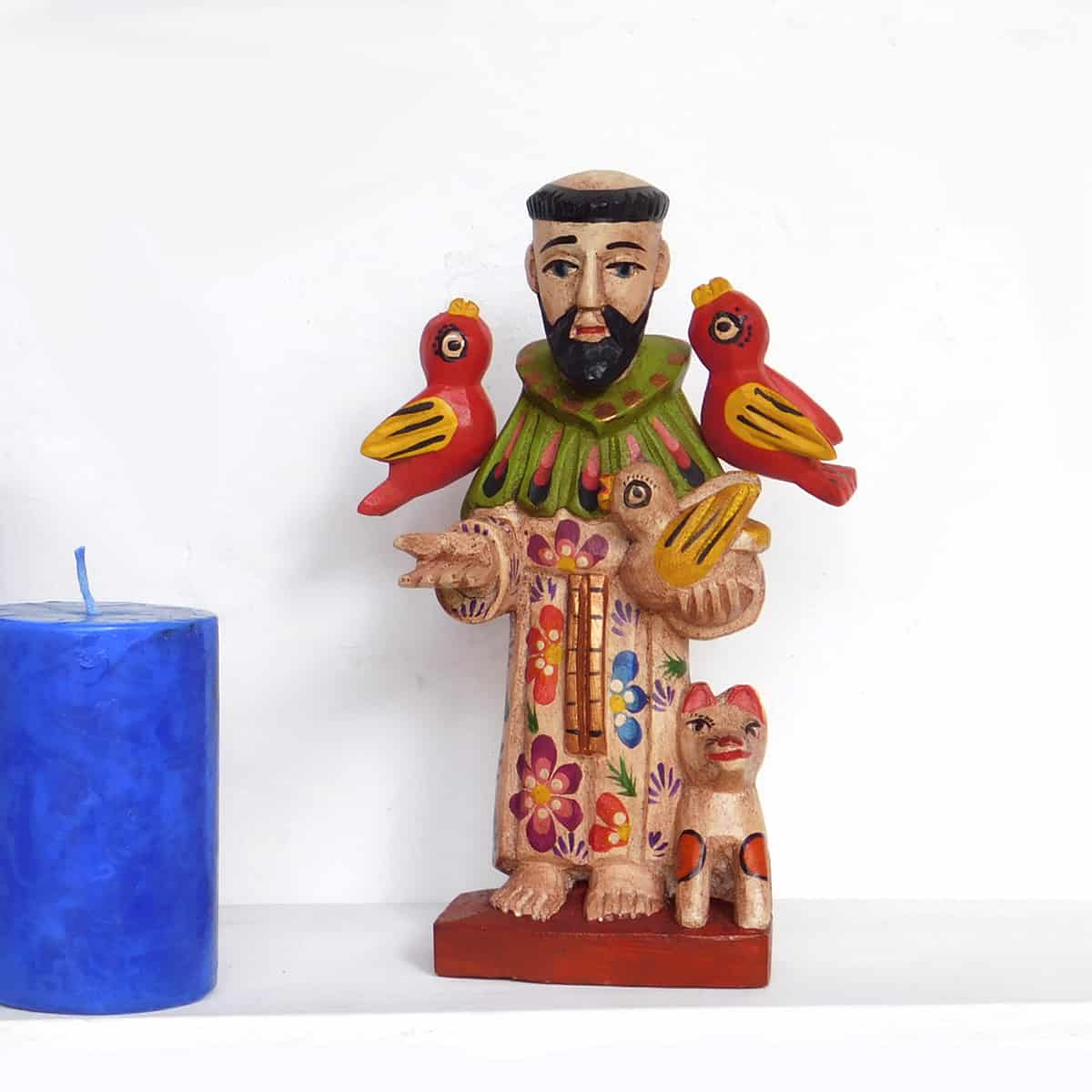 saint francis figurine hand carved and painted in guatemala with three birds and a cat with a blue candle nearby