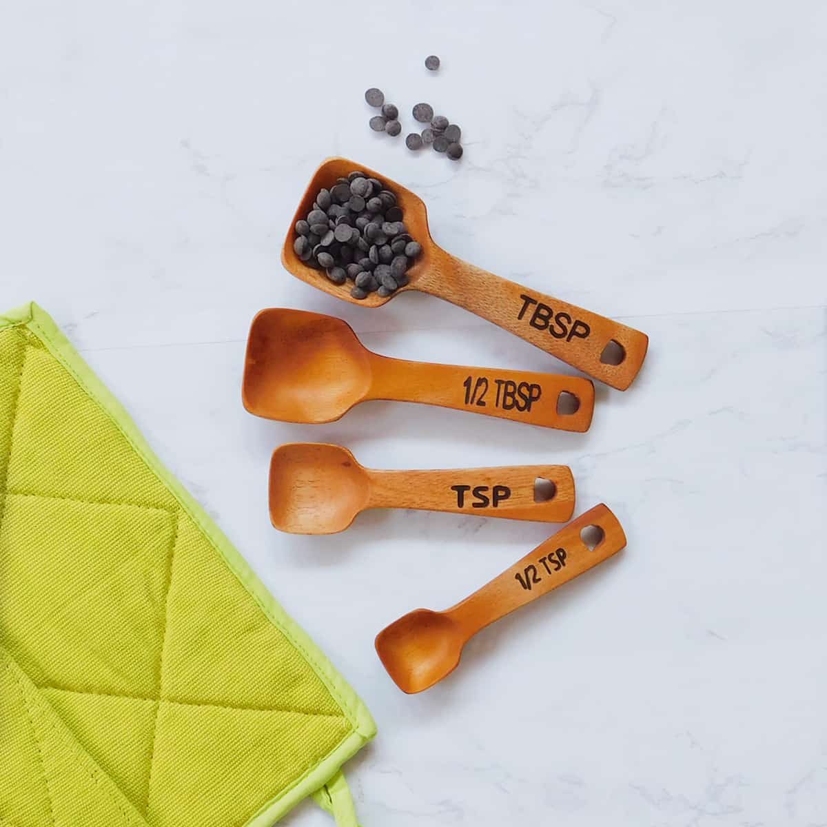 set of 4 wood measuring spoons with chocolate chips on a marble countertop
