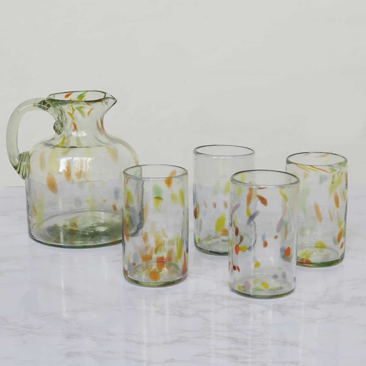 multi colored glassware set with four handblown glasses and a pitcher with colored speckles on white marble