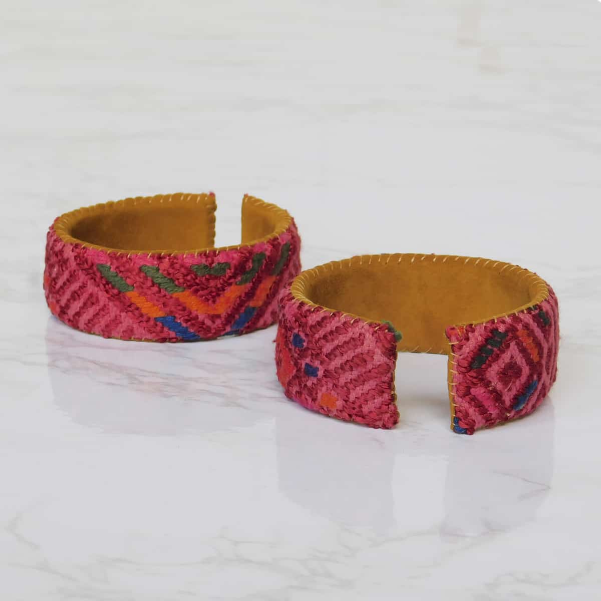 A set of two red cuff bracelets with red woven fabric with diamonds woven onto a leather backing