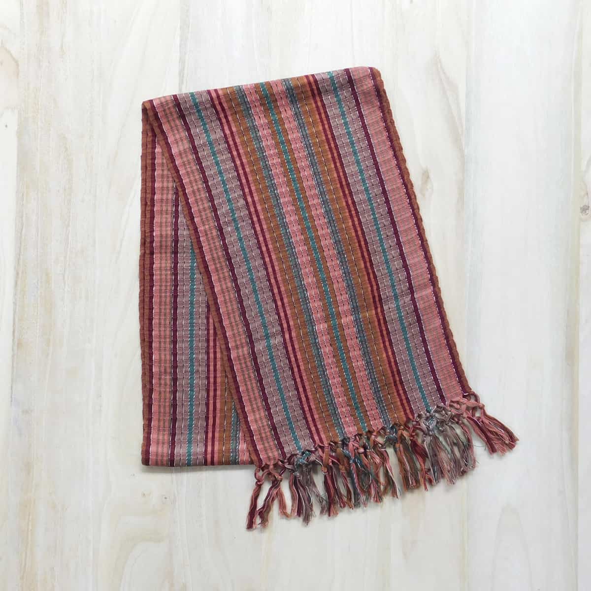A handwoven scarf made in Guatemala with decorative fringe and earth-toned stripes.