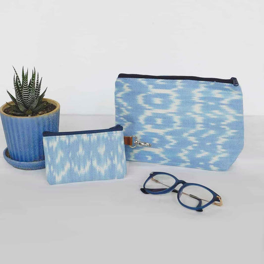 light blue makeup bag and card holder wallet with zippers on a white background with blue glasses and a succulent plant