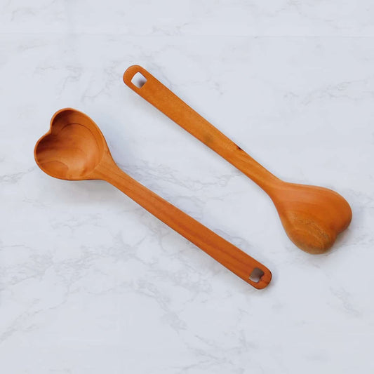 two handmade wooden spoons in the shape of a heart next to one another