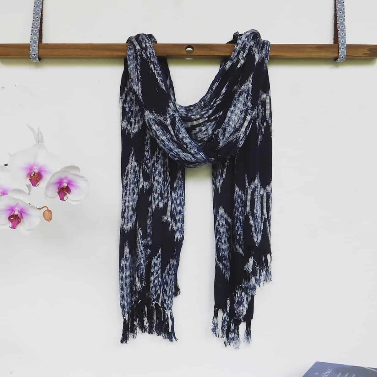 a navy blue and white ikat scarf is draped over a hanging wooden beam next to a pink and white orchid.