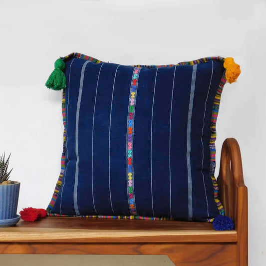 navy blue throw pillow with embroidered decorative brand and different colored tassels on a wooden bench