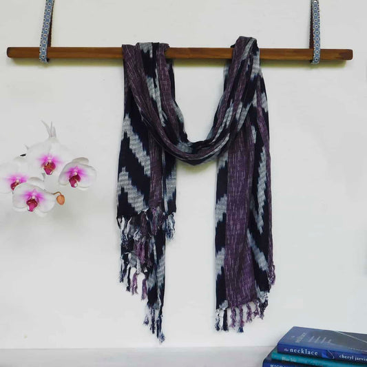  ikat scarf in navy blue and purple draped over a hanging wooden bean next to white lilies