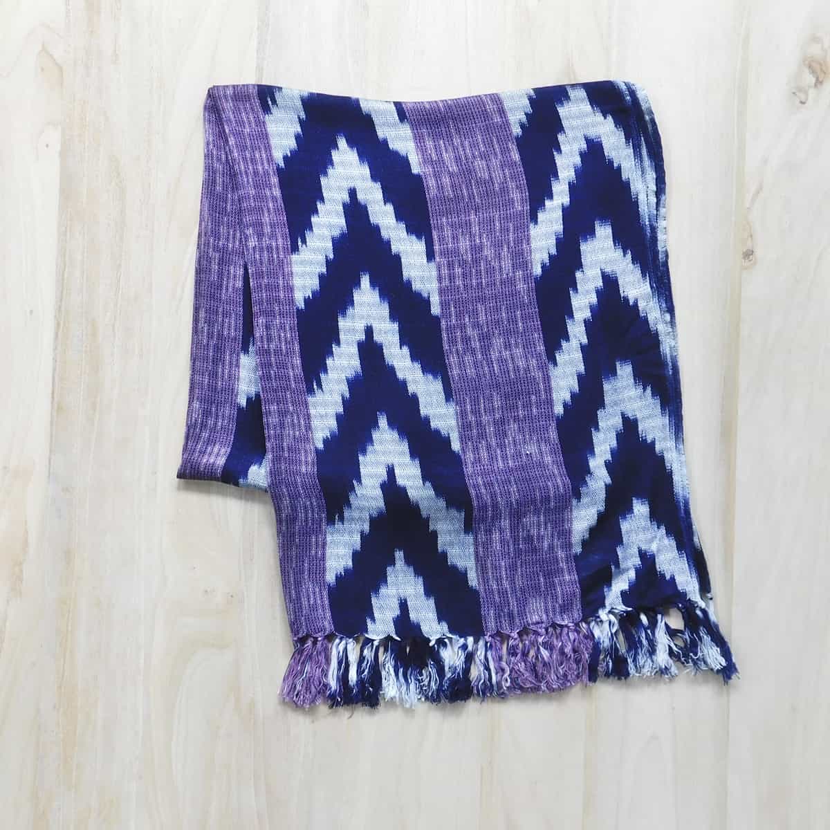 handwoven scarf in navy blue ikat and purple stripes with a decorative fringe on a light wood background