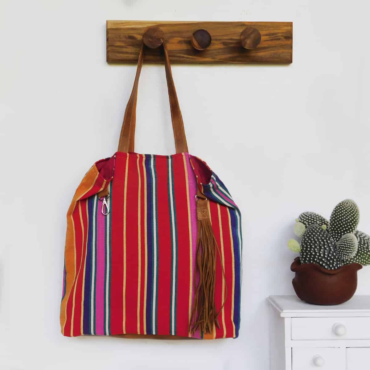 unclasped red tote bag with leather handles and leather tassel hanging next to a cactus plant