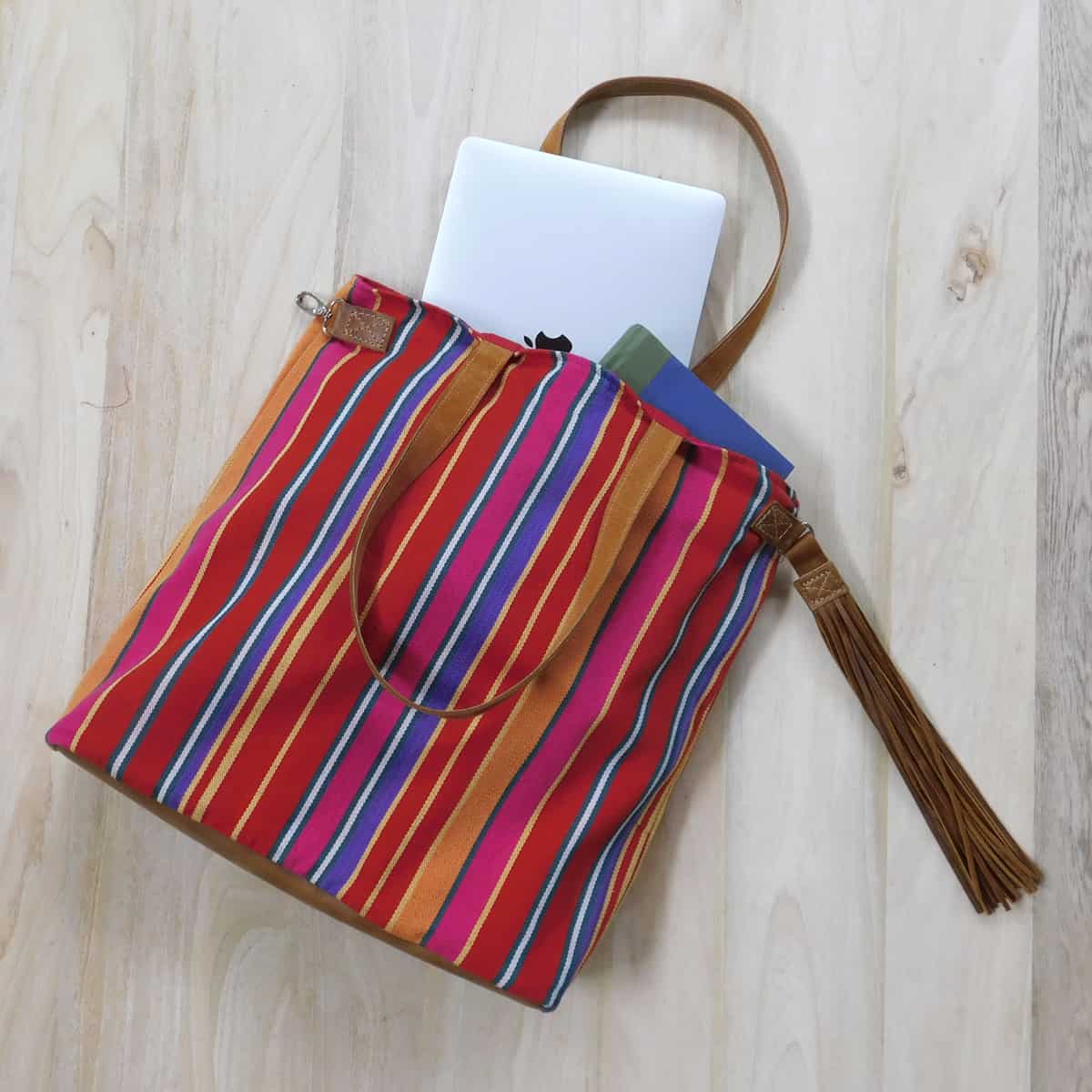 elegant red tote bag on its side with a laptop and a book partially placed inside