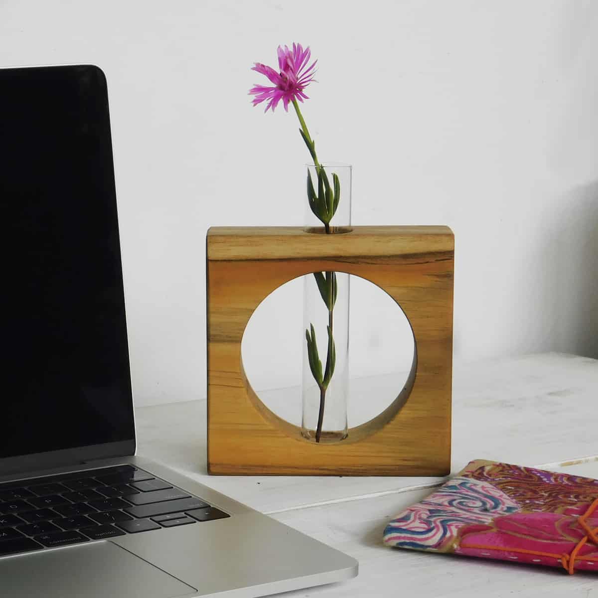 test tube plant holder with a circular wood frame on a desk by a laptop computer and red textile