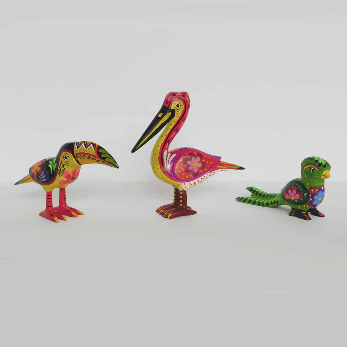 a set of three wild bird figurines standing on a white countertop. they are colorful and stand on their own.